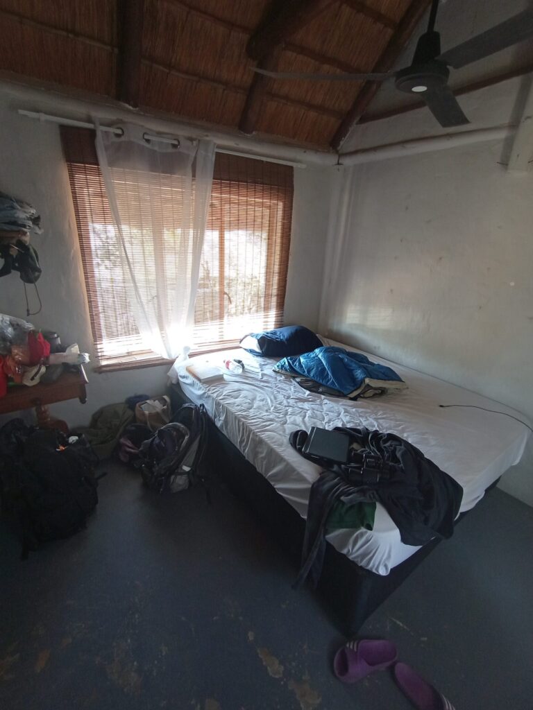 部屋の写真。ベッド、窓、小机があります。雑多なものがあちこちにあり、生活感にあふれています。